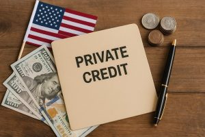 A photograph showing a notebook with the words PRIVATE CREDIT placed on a wooden surface alongside US dollar bills, stacked coins, a black pen with gold accents, and a small United States flag. The scene evokes themes of private credit, finance, economic analysis and investments.